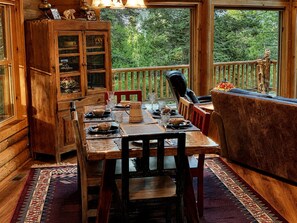 A wooden dining area with a table set for four, a cushioned bench, and a wooden cabinet with glass doors. - Private mountain-top log lodge w/ game room, deck, forest views, near Cloudcroft (Cloudcroft)