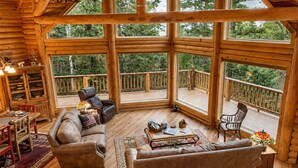 Ein geräumiges Cabin-Interieur mit einer großen Holzdiele, einer gemütlichen Sitzecke inklusive Sofa und Sesseln sowie einem Esstisch mit Stühlen.