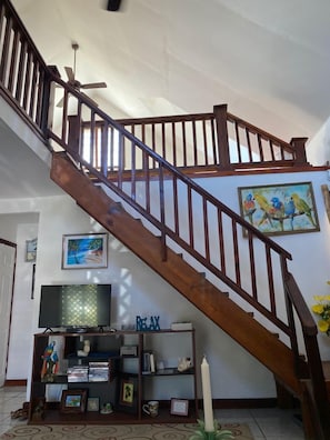 Staircase leads to an upper floor, with a bookshelf below featuring a collection of books and decorative items.