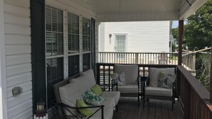 Een overdekt terras met een witte balustrade, een wit gebouw op de achtergrond, en een kleine tafel met stoelen.