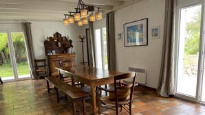 A dining area with a wooden table and benches, a chandelier, and a view of the outdoors through large windows. - Pretty house in a large garden / town center,  (La Flotte)
