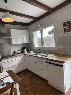 Une cuisine avec des armoires blanches, un plan de travail en bois, une fenêtre et un luminaire suspendu.