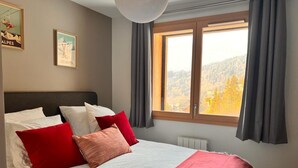 A bedroom with a bed, pillows, a window with curtains, and two framed pictures on the wall.