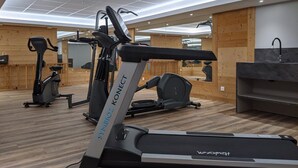 A modern gym with multiple cardio machines, including a treadmill and elliptical, in a spacious room with wooden accents and a large mirror.