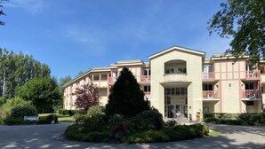 Um hotel de vários andares com entrada central, varandas e um jardim bem cuidado.