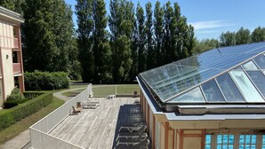 Terraço no telhado com estrutura de vidro, piscina e um edifício com varanda.