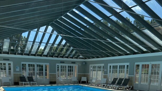 Piscina com teto de vidro, água azul cristalina e interior banhado pelo sol.