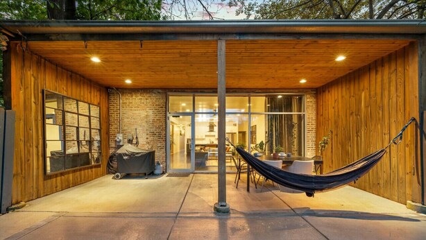 En overdækket terrasse med hængekøje, grill og spiseplads med bord og stole.