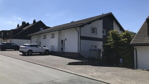 Eine Wohnstraße mit Häusern, einem weißen Auto, das am Straßenrand geparkt ist, und einem strahlend blauen Himmel.