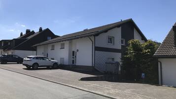 Eine Wohnstraße mit Häusern, einem weißen Auto, das am Straßenrand geparkt ist, und einem strahlend blauen Himmel.