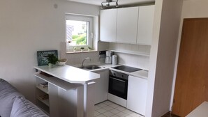 Eine kleine Küche mit weißen Schränken, einem Backofen, einem Spülbecken und einem Fenster mit Pflanzen.