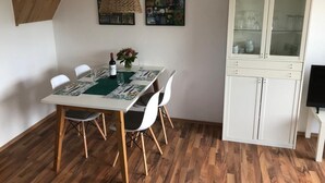 Ein Essbereich mit einem Holztisch, weißen Stühlen, einer Vitrine und zwei gerahmten Kunstwerken an der Wand.