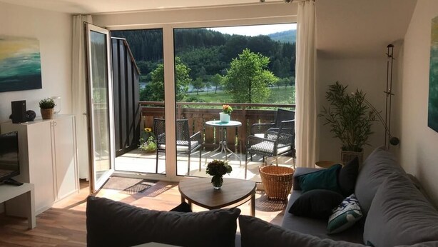 Ein modernes Wohnzimmer mit einer Couch, einem Couchtisch und einem Balkon mit Gartenmöbeln.