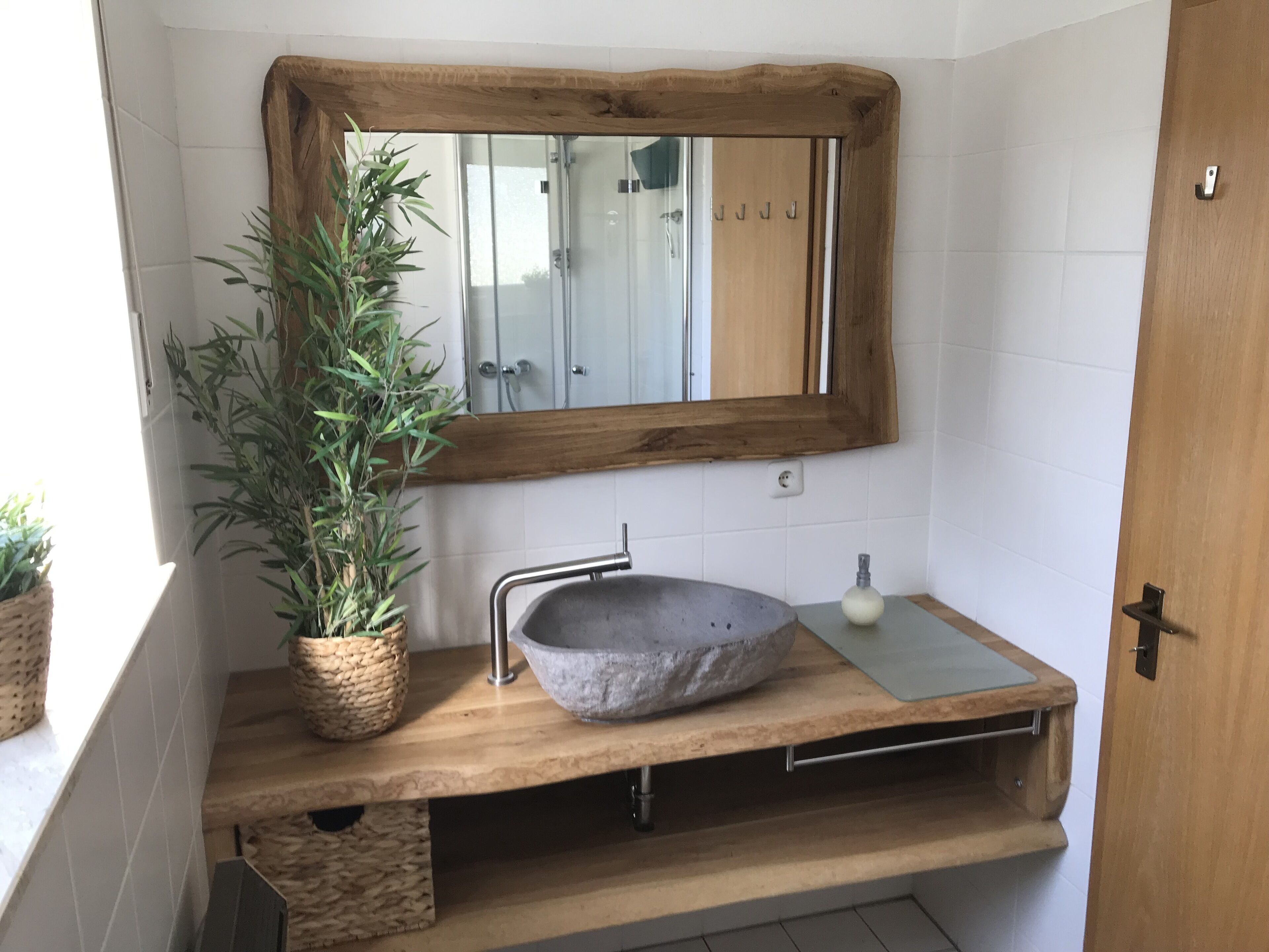 Een badkamer met een houten wastafelmeubel, een stenen wastafel, een spiegel met houten lijst en een potplant.