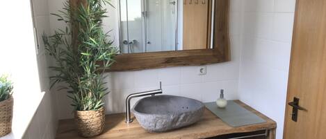 Een badkamer met een houten wastafelmeubel, een stenen wastafel, een spiegel met houten lijst en een potplant.