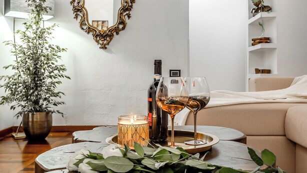 Un salón acogedor con una planta en maceta, una vela, botellas de vino y copas sobre una bandeja.