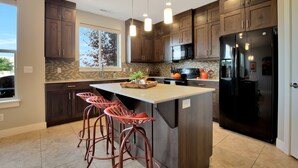 A modern kitchen with dark wood cabinets, a large black refrigerator, and a central island with stools. - Entrada at Moab 598 and 602 | Townies | Pool/Spa | Garage | Same Day Booking (Moab)