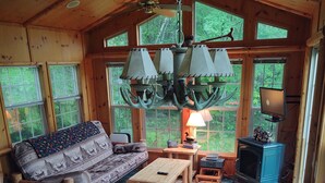 L’intérieur chaleureux d’un chalet comprend un canapé, une table à manger, des chaises, une cheminée et de grandes fenêtres donnant sur la forêt.