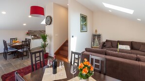 Un salon moderne avec un canapé marron, une table à manger avec des chaises, un luminaire suspendu rouge et un escalier menant à un espace cuisine.