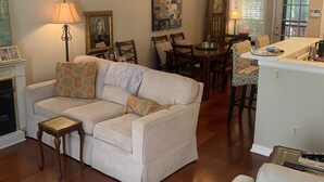 Uma sala de estar com sofá, uma mesa de centro e um espaço de jantar com cadeiras e um candelabro.
