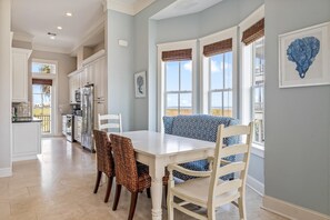 Une cuisine avec des meubles blancs, une table à manger avec des chaises et une vue par les fenêtres.