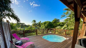 A wooden deck with a hot tub, two pink lounge chairs, and a wicker sofa.