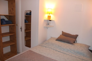A bedroom with a bed, a bedside lamp, a wooden wardrobe, and a mirror.