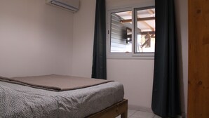 A bedroom with a bed, an air conditioning unit, a window with curtains, and a view of an outdoor area.