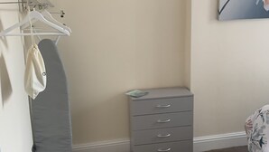 Un dormitorio en esquina con un aparador gris, una percha para ropa y una mesita de noche pequeña.