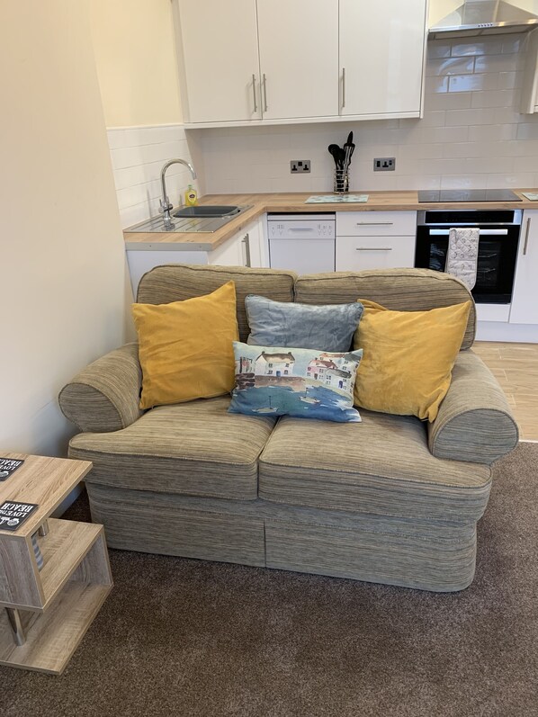 A modern living room with a grey sofa, two mustard-colored pillows, and a small wooden side table.