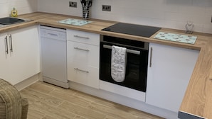 Una cocina moderna con armarios blancos, lavavajillas, horno y campana extractora de acero inoxidable.