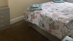 Un dormitorio con cama, cómoda, un cuadro de flores y una ventana con cortinas.