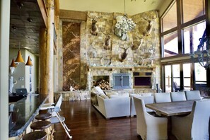 Amplia sala de estar con chimenea de piedra, sofás blancos y una gran mesa de madera.