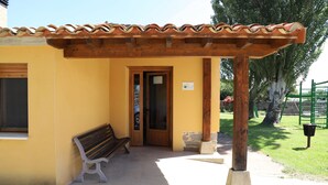 Ein gelbes Gebäude mit einer Holzpergola, einer Bank und einer Tür.