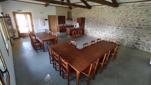 Ein geräumiger Essbereich mit einem großen Holztisch und Stühlen, eine Küche mit Steinwänden und eine hohe Decke mit freiliegenden Balken.