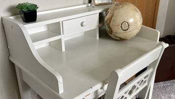Una scrivania in legno bianco con un mappamondo, una piccola pianta in vaso e una cornice con un'immagine.