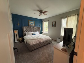 A bedroom with a tufted headboard, a large bed with white bedding, a ceiling fan, and a television on a stand.