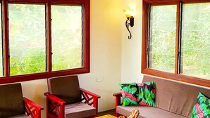 Une pièce dotée d’un ventilateur de plafond, de deux canapés, d’une table basse en bois et de grandes fenêtres donnant sur un paysage verdoyant.