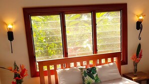 Une chambre à coucher avec un lit en bois, deux tables de chevet, une fenêtre donnant sur un paysage verdoyant et des lampes fixées au mur.