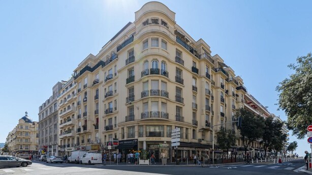 Un hotel de varios pisos con fachada curva, balcones y un café en la planta baja.