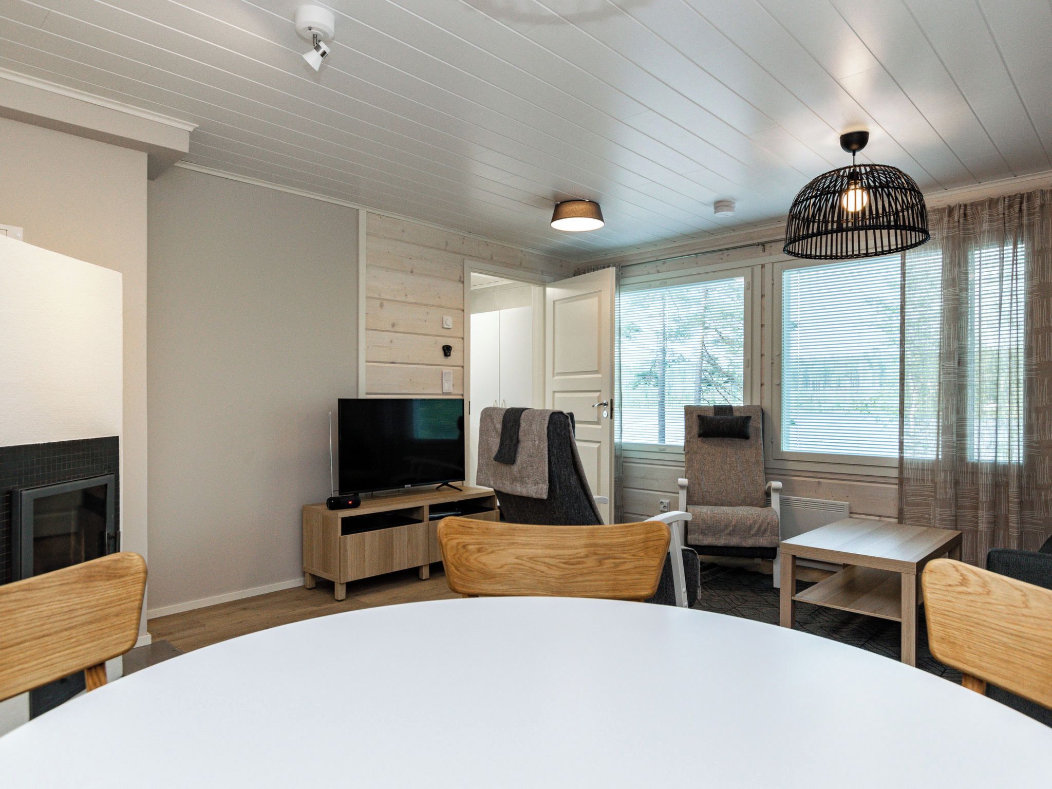 A modern living room with a flat-screen TV, wooden furniture, and large windows.