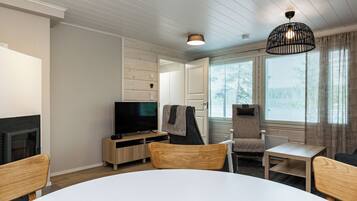 A modern living room with a flat-screen TV, wooden furniture, and large windows.