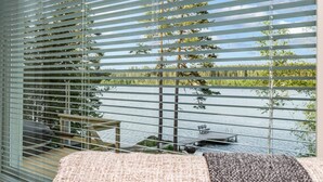 Een kamer met uitzicht op een meer, met horizontale zonwering, een houten terras en tuinmeubilair.