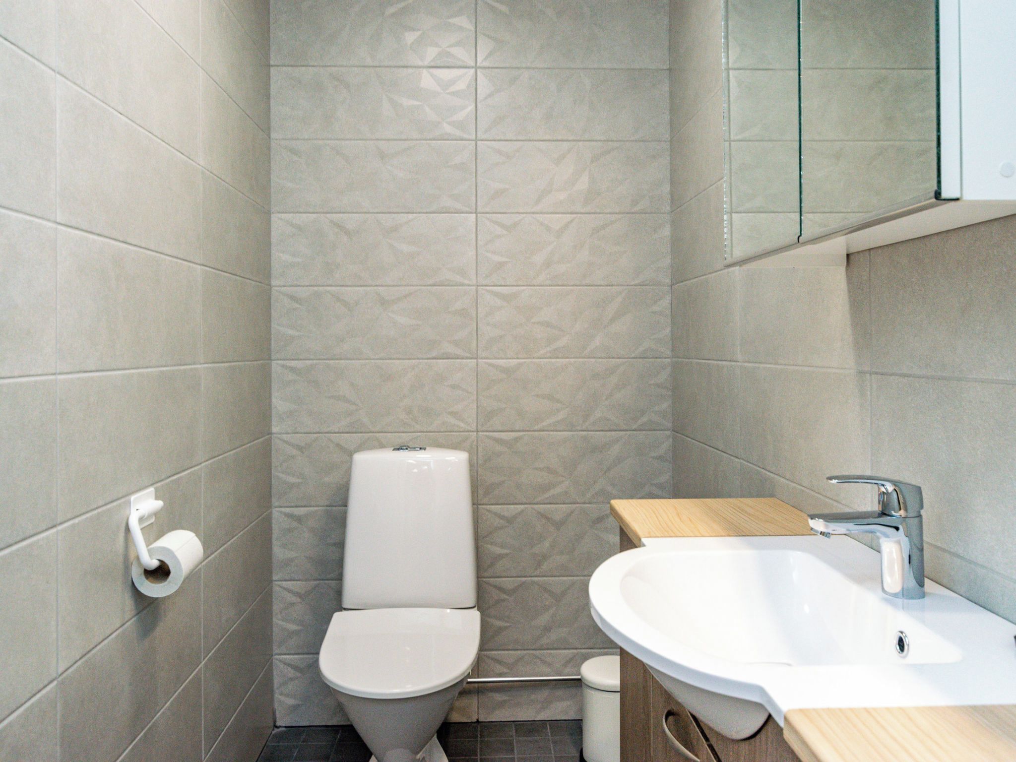 Ein kleines Badezimmer mit Toilette, Waschbecken und Toilettenpapierhalter an der Wand.