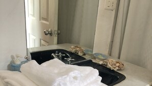 Une salle de bain avec un lavabo blanc, un miroir et un porte-serviettes sur lequel sont pliées des serviettes.