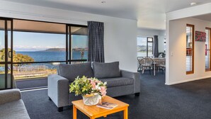 Un salon moderne avec un canapé gris, une table basse en bois ornée d’un vase de fleurs et une vue sur la mer grâce à de grandes fenêtres.