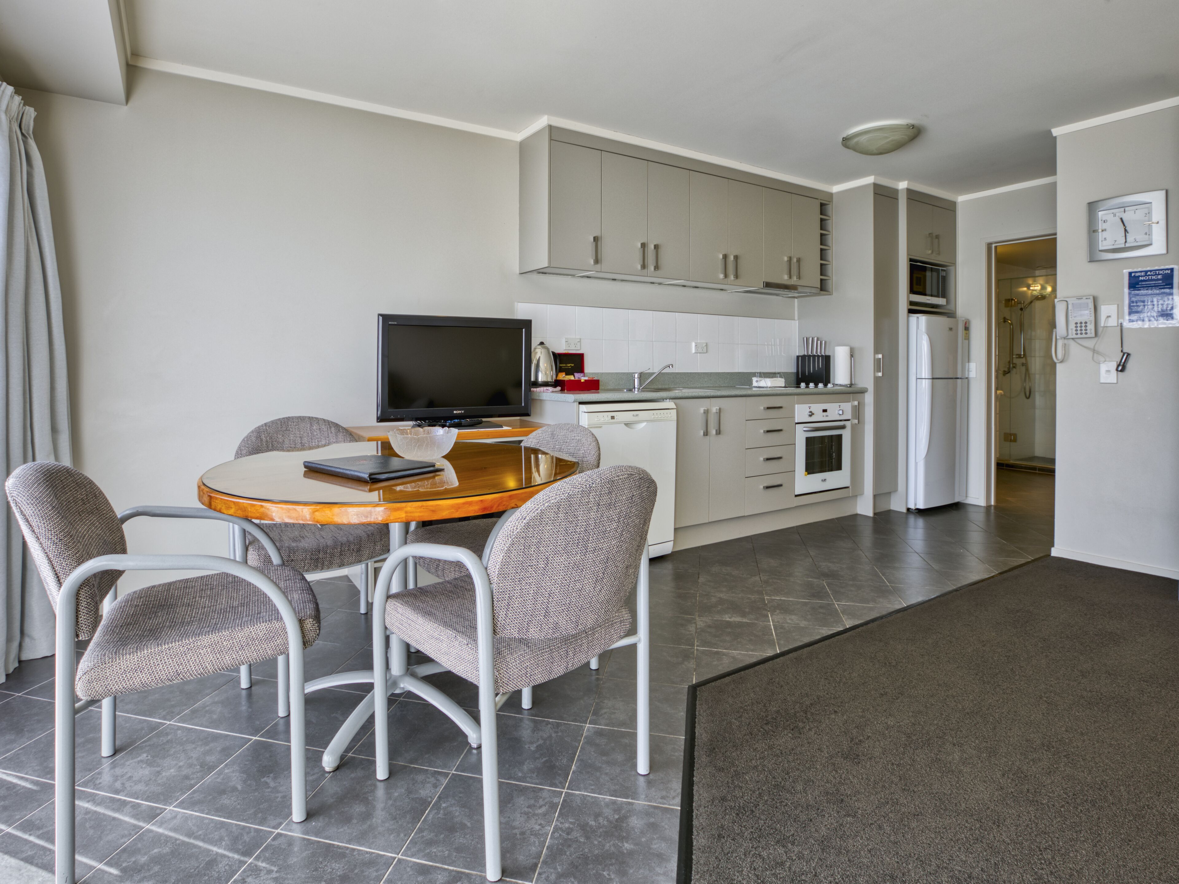 A modern kitchen with a dining area, including a table with chairs, a television, and a refrigerator.