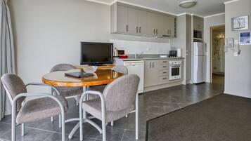 A modern kitchen with a dining area, including a table with chairs, a television, and a refrigerator.