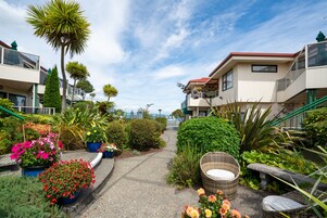 Un sendero conduce a un edificio con balcones, rodeado de macetas con plantas y flores.
