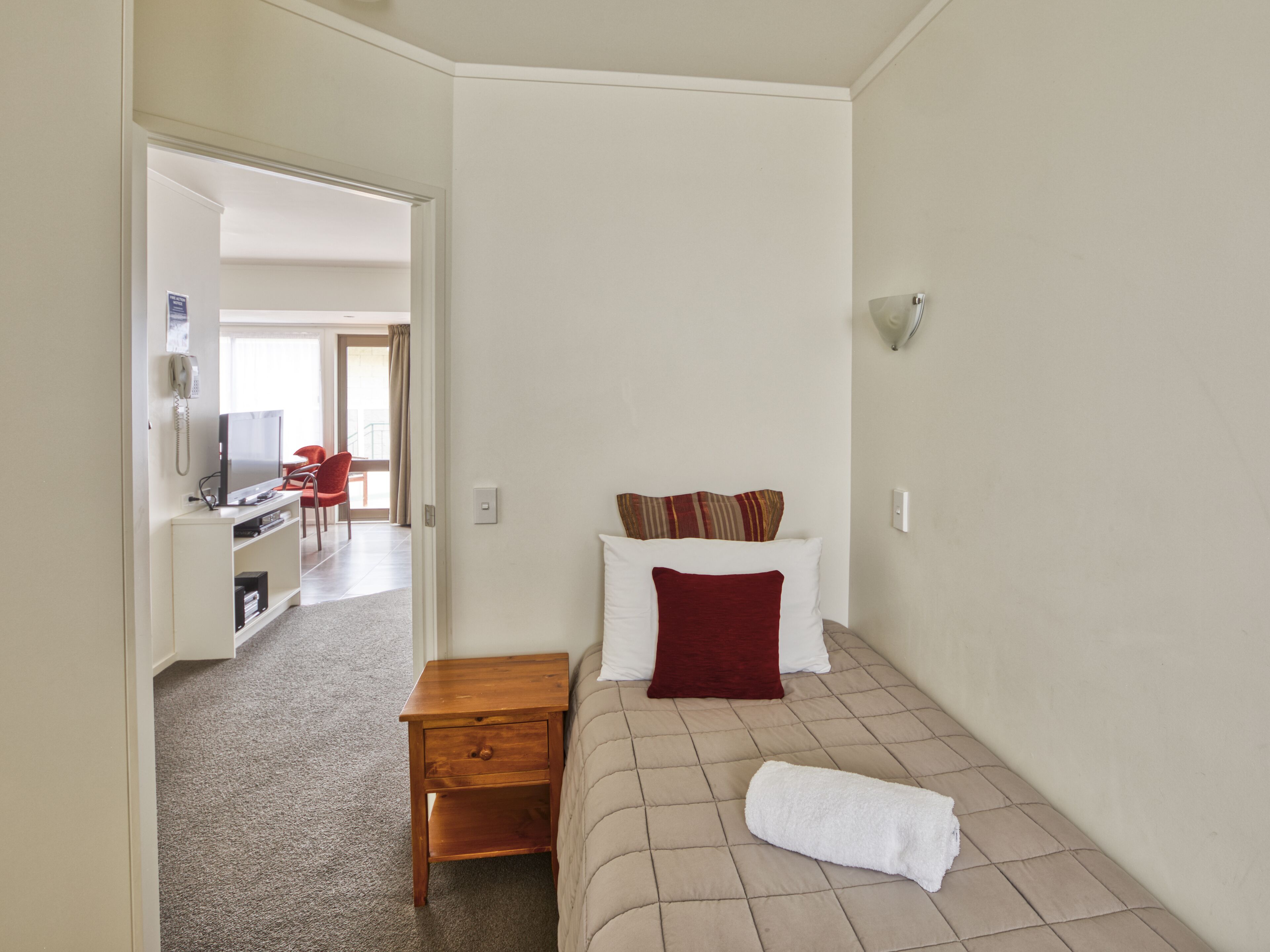 Ein Hotelzimmer mit einem Bett, einem Nachttisch aus Holz, einem Fernseher und einem Schreibtisch mit Stuhl.